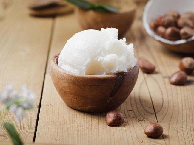 Shea butter in wooden bowl with nuts on old rustic table. Free text space.