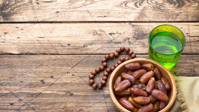 Dried dates fruits and a glass of water on a wooden table. Traditional fast breaking, Muslims evening meal during holy Ramadan