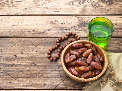 Dried dates fruits and a glass of water on a wooden table. Traditional fast breaking, Muslims evening meal during holy Ramadan