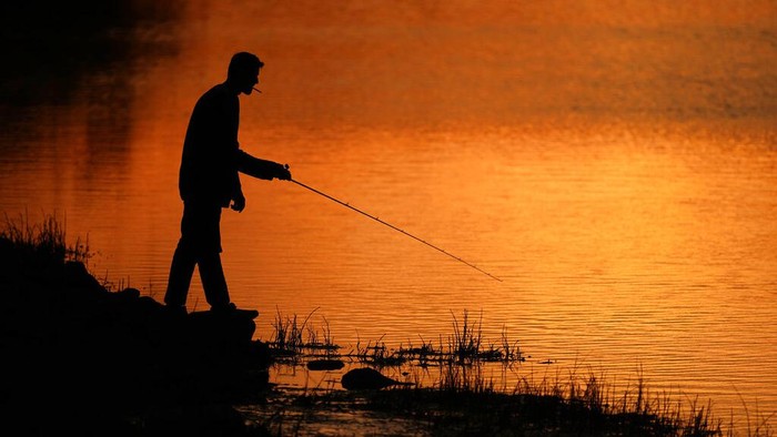 A man fishes at sunset, Tuesday, April 26, 2022, at Shawnee Mission Lake in Shawnee, Kan. (AP Photo/Charlie Riedel)