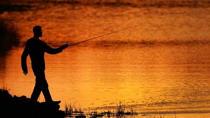 A man fishes at sunset, Tuesday, April 26, 2022, at Shawnee Mission Lake in Shawnee, Kan. (AP Photo/Charlie Riedel)