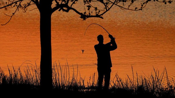Seorang warga terlihat asyik memancing dengan latar belakang berupa lansekap Danau Misi Shawnee dikala senja.