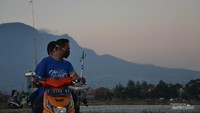 Warga menggunakan motor saat menunggu waktu berbuka puasa sambil membawa alat pancing.