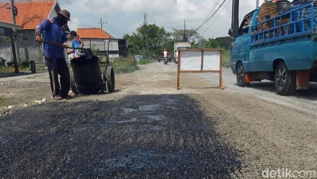 Pekerja melakukan perbaikan jalan rusak di Lamongan.