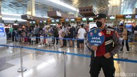 Seorang petugas dengan rambu jaga jarak sigap di antara antrean penumpang, hal ini guna mengingatkan kembali akan protokol kesehatan saat mudik di tengah pandemi corona.