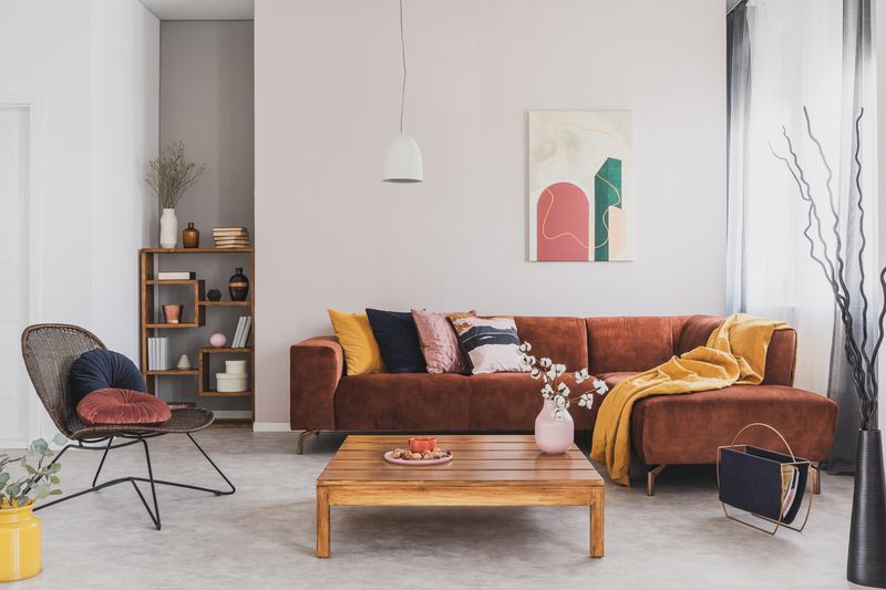 Flowers in vase on wooden coffee table in fashionable living room interior with brown corner sofa with pillows and abstract painting on the wall