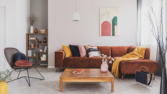Flowers in vase on wooden coffee table in fashionable living room interior with brown corner sofa with pillows and abstract painting on the wall