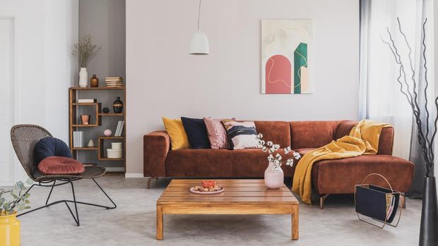 Flowers in vase on wooden coffee table in fashionable living room interior with brown corner sofa with pillows and abstract painting on the wall