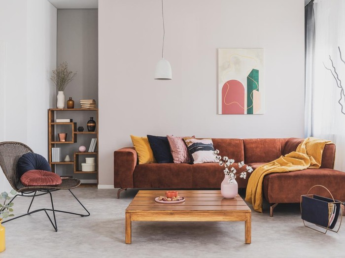Flowers in vase on wooden coffee table in fashionable living room interior with brown corner sofa with pillows and abstract painting on the wall