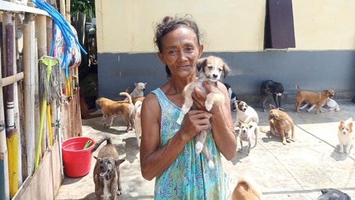 Sumiati sembari memeluk salah satu anjing yang dimilikinya pada Minggu (1/5/2022). Kini Sumiati memiliki 65 anjing yang dirawatnya di rumahnya yang berlokasi di area Pantai Padang Galak, Denpasar