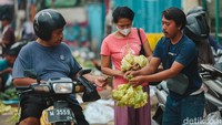 Seorang pedagang kulit ketupat sedang melayani pembeli.