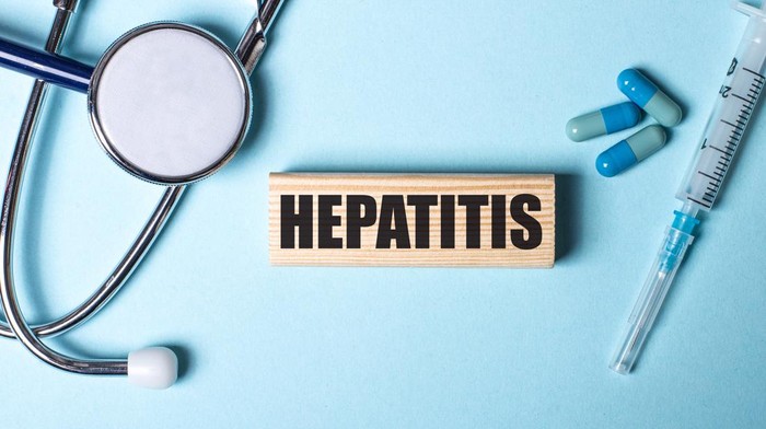 1341701343 HEPATITIS written on a wooden block near a stethoscope, syringe and pills on a blue background. Medical concept
