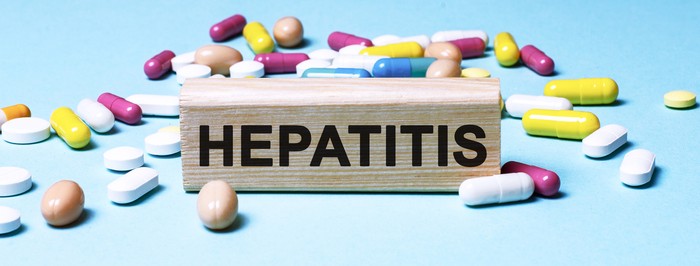 The word Hepatitis is written on wooden blocks next to tablets on a blue background. Medical concept