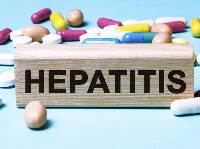 The word Hepatitis is written on wooden blocks next to tablets on a blue background. Medical concept