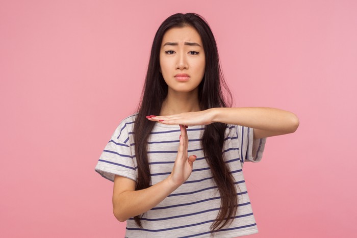 Stop, enough, I need break. Portrait of exhausted girl with long hair in t-shirt showing time-out gesture and looking imploringly, asking for pause. indoor studio shot isolated on pink background