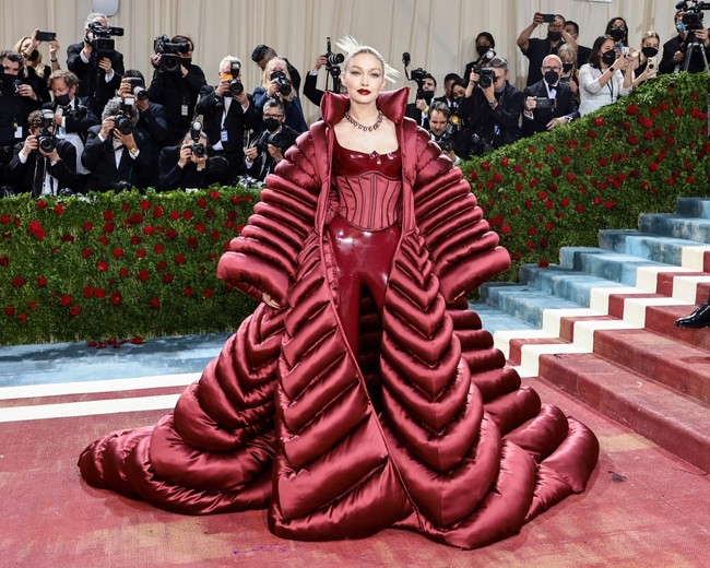 Saat tiba di karpet merah Met Gala 2022, Gigi Hadid menambahkan coat super besar dalam penampilannya. Seluruh busana yang dipakainya ke Met Gala 2022 datang dari brand Versace. Foto: Getty Images via AFP/JAMIE MCCARTHY