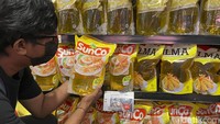 Seorang pembeli mengecek harga dan minyak goreng yang akan dibelinya.
