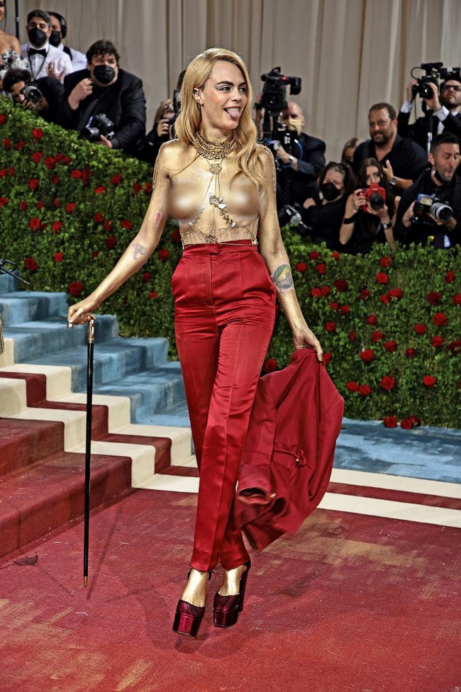 Model dan aktris Cara Delevingne menjelma sebagai manusia emas. Tubuhnya dibungkus setelan merah Dior Haute Couture yang kemudian ia buka bagian blazer bergaya militernya dan tampil topless di sepanjang karpet merah. (Foto: Getty Images via AFP/DIMITRIOS KAMBOURIS)
