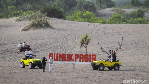 Wisatawan berfoto di papan nama Gumuk Pasir dengan mobil jip.