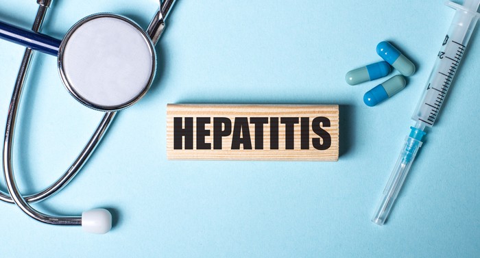 HEPATITIS written on a wooden block near a stethoscope, syringe and pills on a blue background. Medical concept