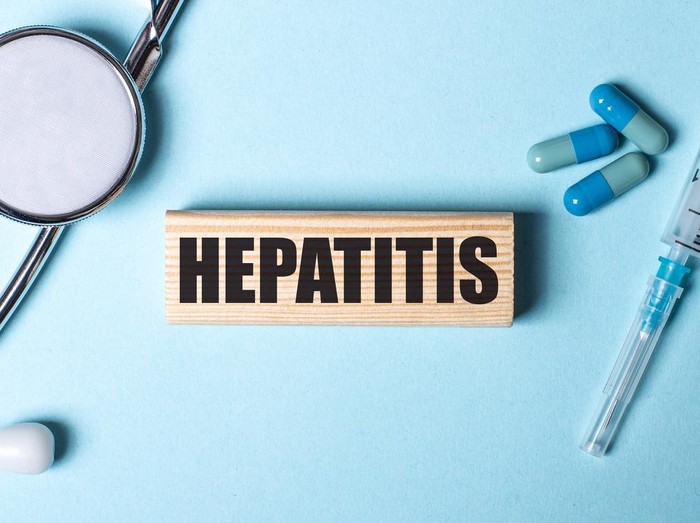 HEPATITIS written on a wooden block near a stethoscope, syringe and pills on a blue background. Medical concept