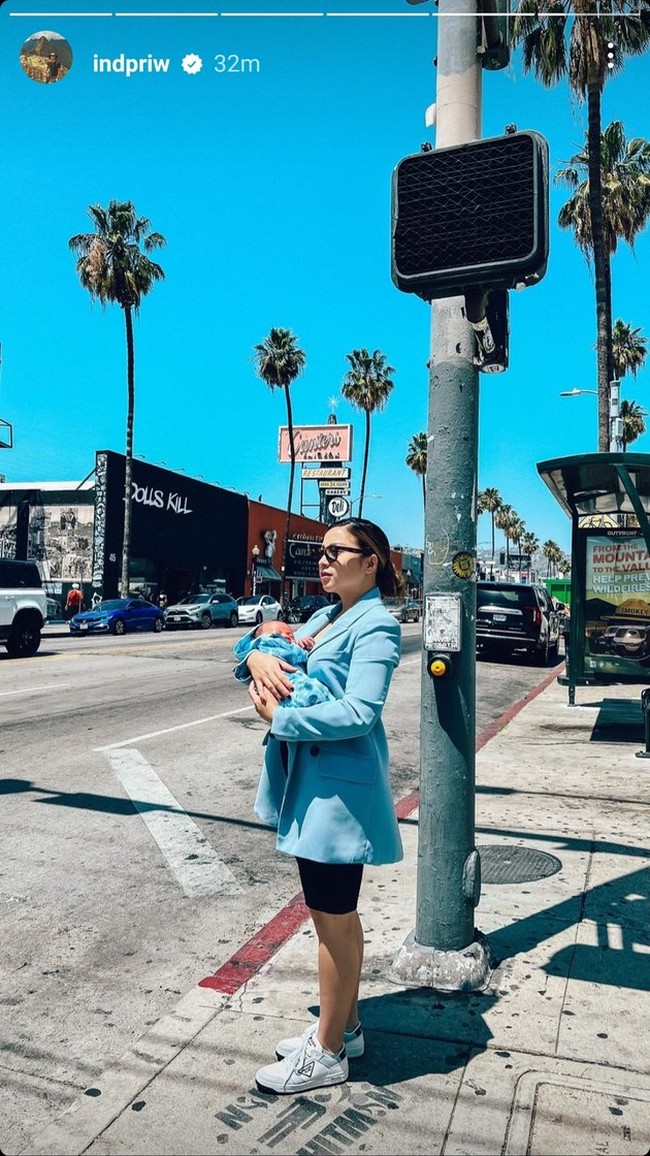 Sambil menggendong sang anak, Nikita Willy tampak stylish mengenakan blazer berwarna biru muda yang dipadukan dengan dalaman dress hitam. Untuk menyempurnakan penampilannya, Nikita mengenakan sneakers putih dan sebuah kaca mata hitam. Foto: Instagram