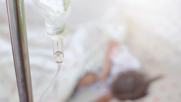 Closeup saline IV drip for patient and Infusion pump feeding into child patient while she is sleeping on bed in the hospital