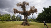 Seorang pria berjalan dengan anjingnya melewati instalasi seni sebuah pohon yang dibuat dengan ratusan sangkar burung di taman Parque do Povo di Sao Paulo, Brasil, Jumat (6/5/2022).  
