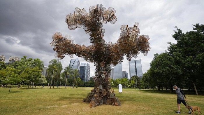 A man walks his dog past an art installation by Brazilian artist Eduardo Srur depicting a tree made with hundreds of bird cages seized by the environmental police from animal traffickers at the Parque do Povo park in Sao Paulo, Brazil, Friday, May 6, 2022. According to the artist, the exhibition 