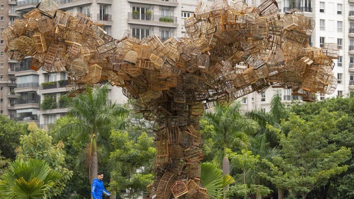 A man walks his dog past an art installation by Brazilian artist Eduardo Srur depicting a tree made with hundreds of bird cages seized by the environmental police from animal traffickers at the Parque do Povo park in Sao Paulo, Brazil, Friday, May 6, 2022. According to the artist, the exhibition 