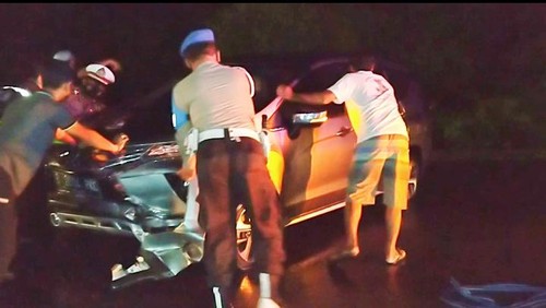 Petugas kepolisian dibantu warga saat mengevakuasi mobil milik wisatawan asal Jakarta yang menabrak median jalan Denpasar - Gilimanuk, Minggu malam (8/5/2022)
