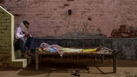 Seorang pria duduk di sebelah istrinya, yang menderita demam tinggi, saat dia secara intravena menerima cairan rehidrasi di klinik darurat selama gelombang penyakit coronavirus di desa Parsaul yang terletak di negara bagian utara Uttar Pradesh, India, 22 Mei, 2021. REUTERS/Adnan Abidi