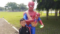 Terlihat patung Spiderman dewasa menggendong Spiderman kecil. Menariknya dia menggunakan kain bermotif batik. Tangan kanan Spiderman memegang di bayi, sedangkan tangan kirinya memegang semangkok makanan bayi. (Ito Septiono/Instagram)