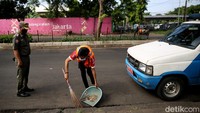 Petugas Satpol PP memantau warga yang tengah menyapu jalan sebagai hukuman karena tak mengenakan masker saat beraktivitas di luar rumah.