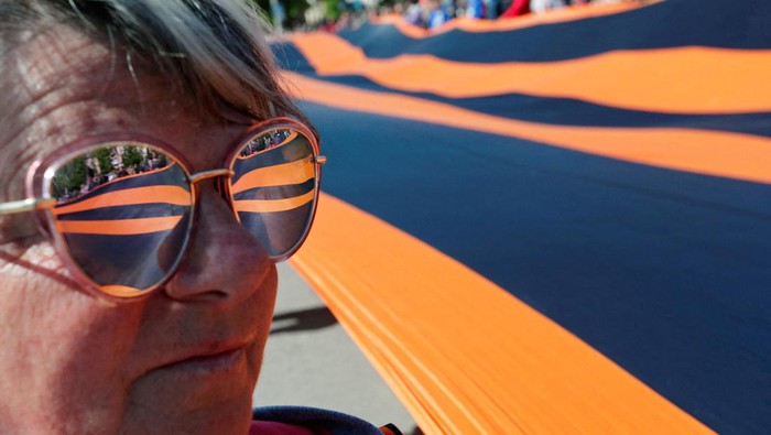 Warga Pro-Rusia Merayakan Hari Kemenangan di Mariupol A participant stands next to a giant St. George's Ribbon during a ceremony, marking the 77th anniversary of the victory over Nazi Germany in World War Two, in the course of Ukraine-Russia conflict in the southern port city of Mariupol, Ukraine May 9, 2022. REUTERS/Alexander Ermochenko TPX IMAGES OF THE DAY