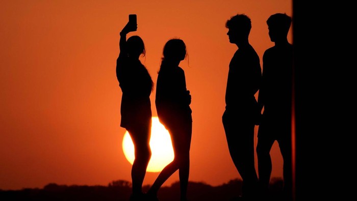 A woman is silhouetted against the sky as the sun sets Wednesday, May 11, 2022, in Kansas City, Mo. Sunsets have been more vibrant than normal as smoke from a large wildfire in New Mexico drifts eastward across the midwest. (AP Photo/Charlie Riedel)