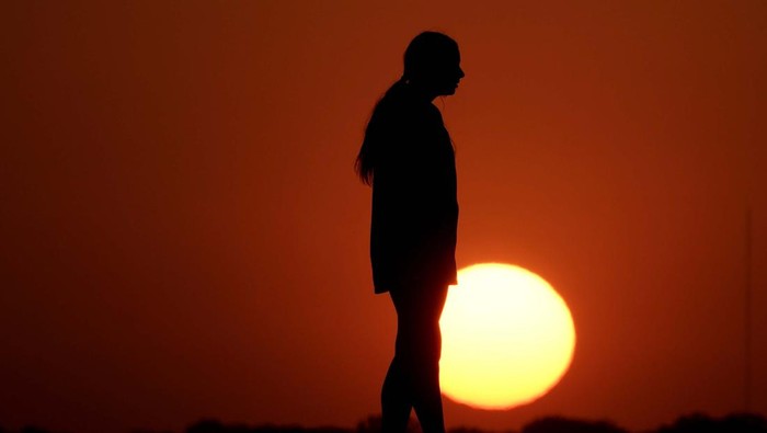 A woman is silhouetted against the sky as the sun sets Wednesday, May 11, 2022, in Kansas City, Mo. Sunsets have been more vibrant than normal as smoke from a large wildfire in New Mexico drifts eastward across the midwest. (AP Photo/Charlie Riedel)