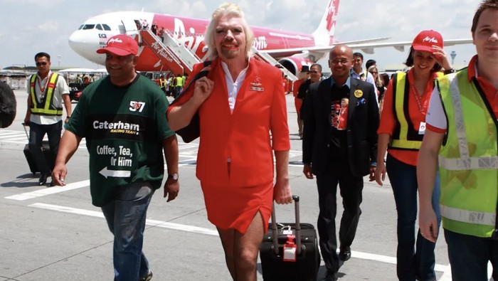 Jutawan nyentrik pemilik maskapai Virgin Airlines, beraksi gila-gilaan saat menjadi pramugari waria dalam penerbangan amal AirAsia. Dia menumpahkan minuman ke baju bos AirAsia dan pamer stocking di depan muka penumpang.