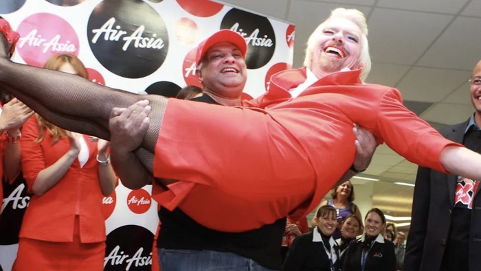 Jutawan nyentrik pemilik maskapai Virgin Airlines, beraksi gila-gilaan saat menjadi pramugari waria dalam penerbangan amal AirAsia. Dia menumpahkan minuman ke baju bos AirAsia dan pamer stocking di depan muka penumpang.