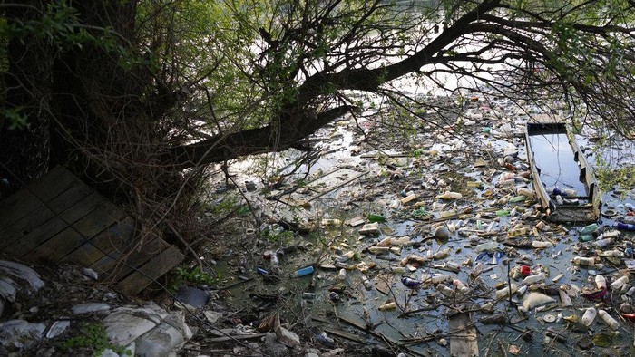 Serbia Darurat Sampah! A man walks between sunken boats, plastic bottles and waste at the Danube river in Belgrade, Serbia, Monday, May 10, 2022. (AP Photo/Darko Vojinovic)