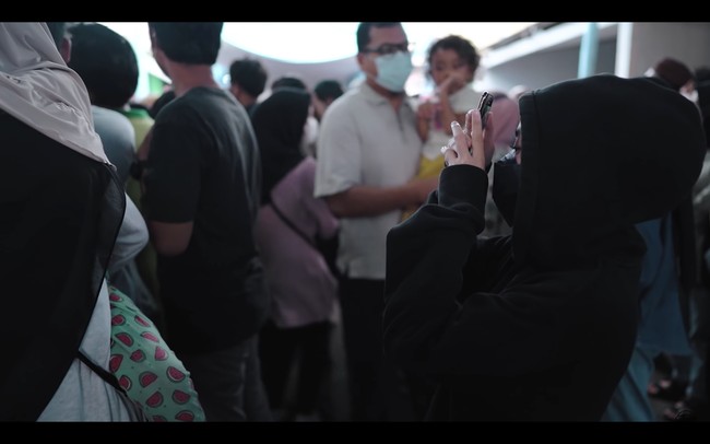 Ternyata Nissa Sabyan dan rekannya sudah menyiapkan kejutan untuk warga RW 01 Jaticempaka. Dia sengaja berjalan dari belakang panggung memakai hoodie hitam untuk merahasiakan identitasnya. Meskipun banyak yang berlalu-lalang, penyamarannya berhasil hingga naik ke atas panggung. Foto: dok. YouTube SABYAN