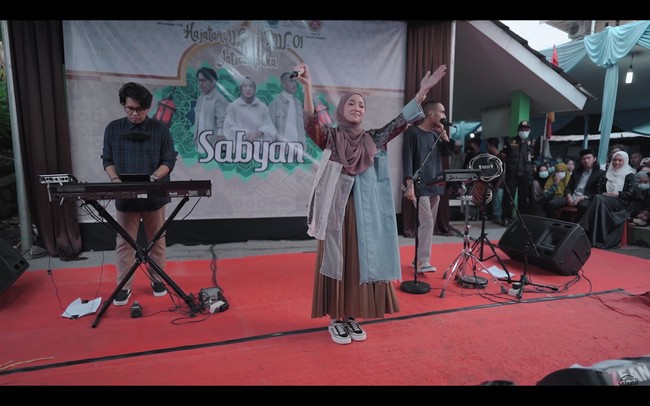 Penampilan Nissa Sabyan di acara hajatan itu pun terbilang unik. Nissa memakai gamis bercorak merah yang dipermak ulang. Ada tambalan yang menyerupai celana jeans pada bagian kanan depan, lengkap dengan sakunya. Foto: dok. YouTube SABYAN