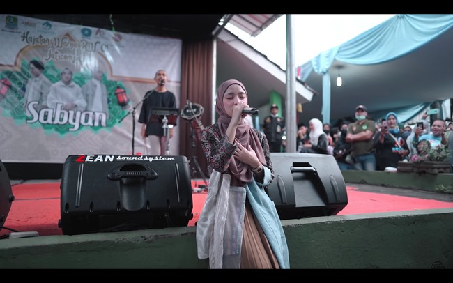 Warga kampung ikut bernyanyi bersama Nissa Sabyan saat menyanyikan lagu Aisyah Istri Rasulullah. Dia semakin dekat dengan penonton saat duduk di pinggir panggung. Foto: dok. YouTube SABYAN
