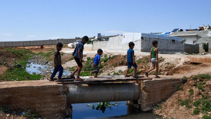 1240728249 Camp children play on the wall separating Syria and Turkey near the town of Atma in Idlib countryside, northwest of Syria, on May 17, 2022. (Photo by Rami Alsayed/NurPhoto via Getty Images)