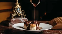Terakhir ini tampilan menu gelato vanilla nya yang legendaris, disajikan dengan saus cokelat lumer dan potongan kue di atasnya.  Foto: Le Procope/The Fork
