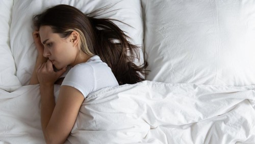 Top view of anxious young woman lying alone in bed thinking pondering of relationship problems, worried millennial female rest in bedroom lost in thoughts after divorce or breakup, loneliness concept