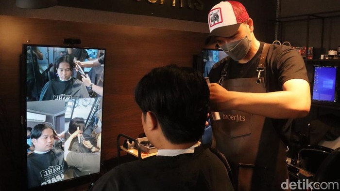 Customer di Barberfits Bandung sedang dilayani potong rambut melihat cermin canggih yang terhubung dengan tiga kamera.