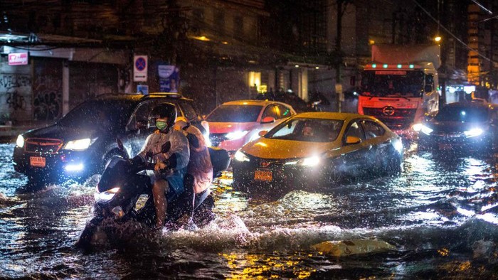 Potret Banjir di Bangkok Usai 10 Jam Diguyur Hujan TOPSHOT - Waste disposal workers wear ponchos as they ride down a flooded street after heavy rain in Bangkok on May 18, 2022. (Photo by Jack TAYLOR / AFP) (Photo by JACK TAYLOR/AFP via Getty Images)