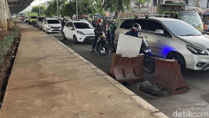 Sebuah lubang menganga di Jalan K.H Noer Alie, Kota Bekasi. Di atas lubang itu terdapat papan bertuliskan 