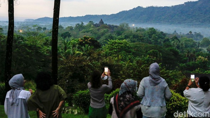 Wisatawan menikmati pemandangan alam dengan latar belakang Candi Borobudur, saat matahari terbit di tempat wisata Bukit Dagi, Borobudur, Jawa Tengah, Jumat (20/5/2022). Terletak di ketinggian 275 meter, Bukit Dagi merupakan tempat terbaik di Borobudur untuk menikmati pemandangan matahari terbit dan keindahan Candi Borobudur.